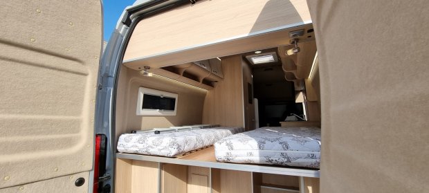 Wnętrze kampera z tylnymi łóżkami, drewnianymi szafkami i półkami pod sufitem