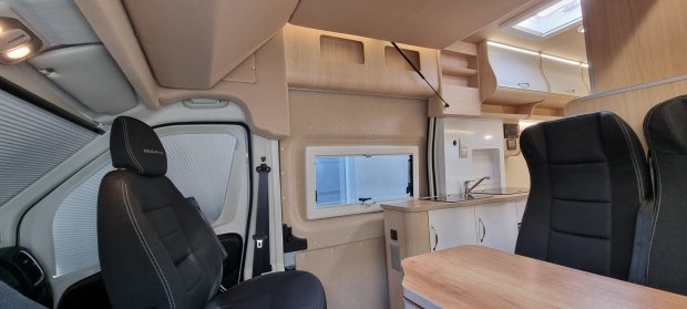 Wnętrze kampera: fotele, drewniana kuchnia z umywalką i boczne okno.