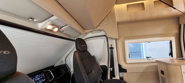 Wnętrze kampera z przednim fotelem, zasłoniętymi roletami i małym oknem.