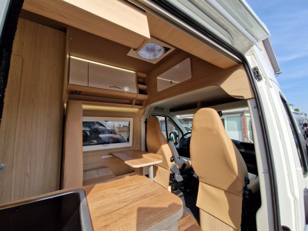Wnętrze kampera z drewnianą zabudową, stolikiem i obróconymi przednimi fotelami