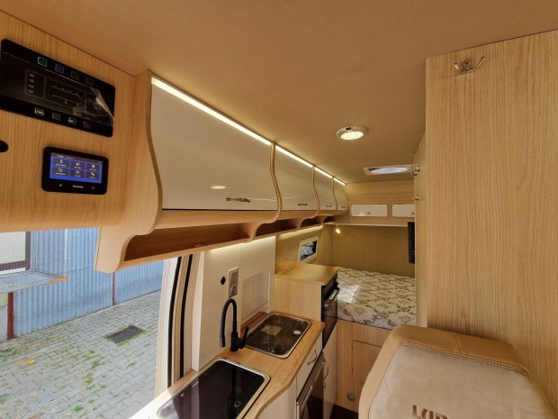 Wnętrze kampera: drewniana kuchnia z zlewem i płytą, górne szafki i łóżko