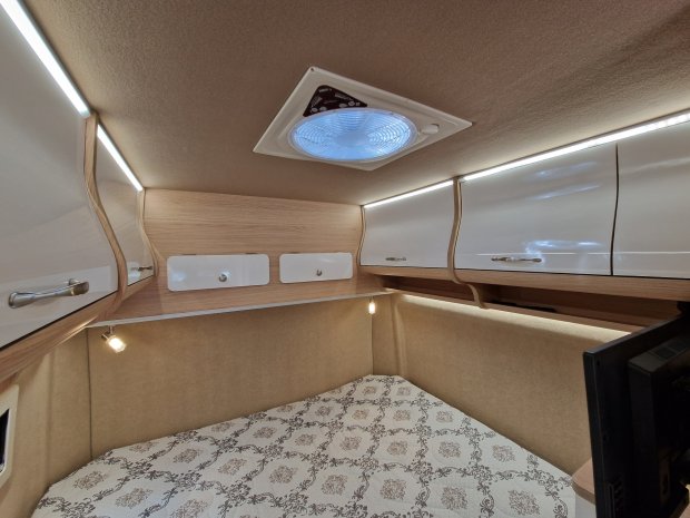 Wnętrze kampera: łóżko z wzorzystą pościelą, białe lakierowane szafki, sufitowy wentylator