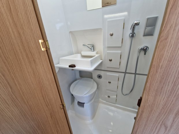Mała łazienka w kamperze z toaletą, umywalką i prysznicem ręcznym.