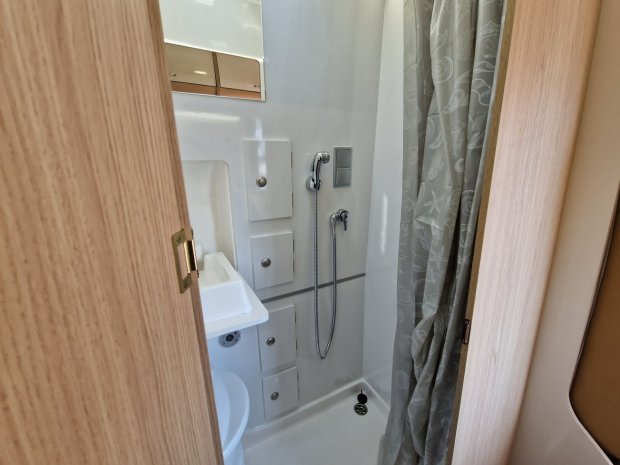 Kompaktowa łazienka kampera z kabiną prysznicową, natryskiem ręcznym, umywalką i zasłoną.