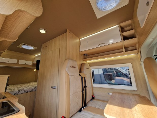 Wnętrze kampera z drewnianymi szafkami, dwoma fotelami, stołem i łóżkiem