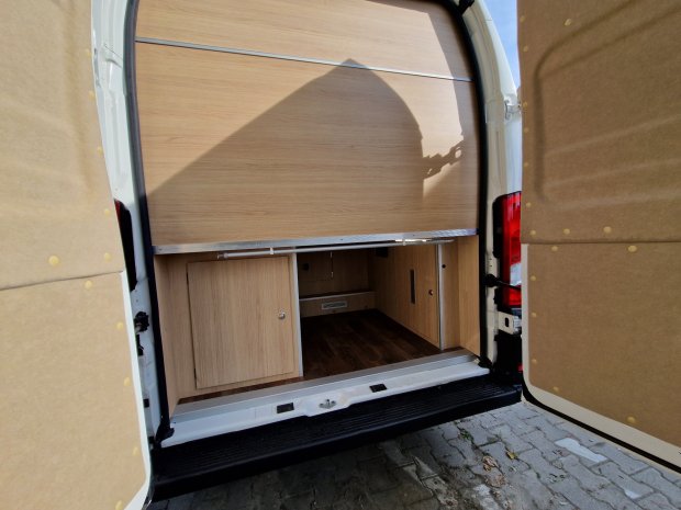 Otwarty tył białego vana z wnętrzem wyłożonym drewnianymi panelami i schowkami.