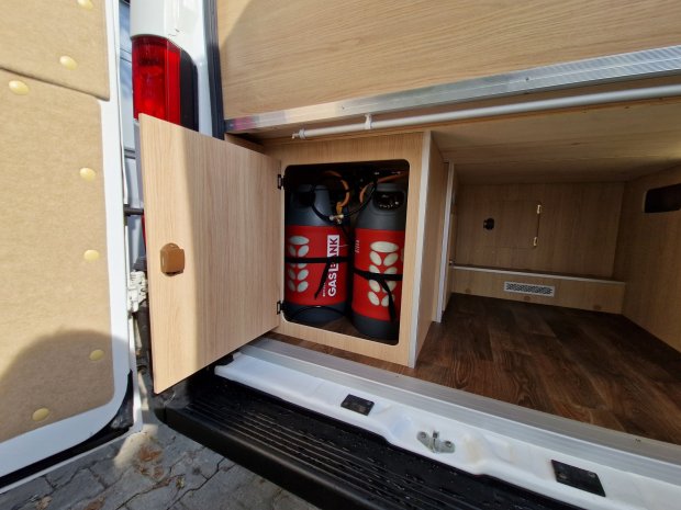 Otwarty schowek w samochodzie kempingowym z dwiema czerwonymi butlami gazowymi