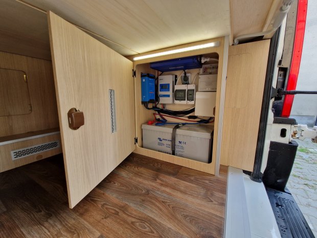 Otwarta szafka w kamperze z akumulatorami i modułami elektrycznymi