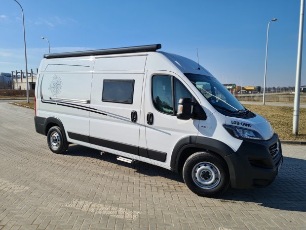 Biały kamper LUB-CAMP zaparkowany na brukowanym placu w słoneczny dzień