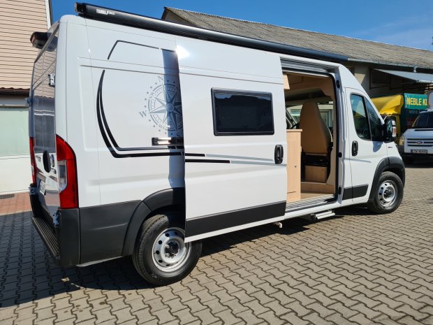 Biały kamper z otwartymi drzwiami przesuwnymi i motywem kompasu, zaparkowany.