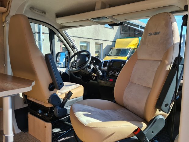 Wnętrze kampera z obrotowymi beżowymi fotelami i deską rozdzielczą.