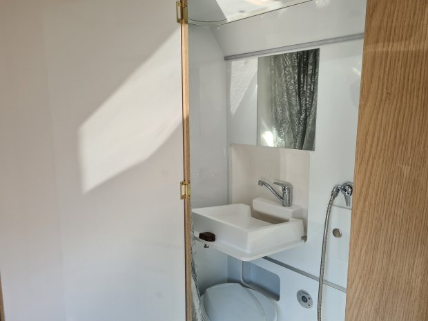 Mała łazienka kampera: zlew z kranem, lustro, prysznic i toaleta przy drewnianych drzwiach