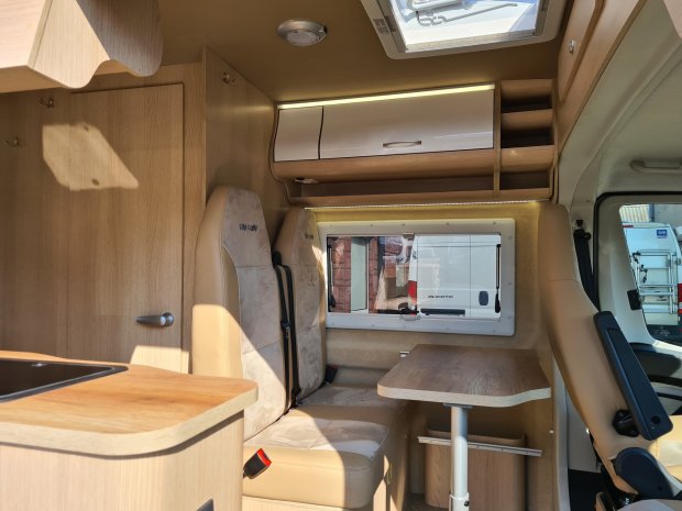 Wnętrze kampera: jasne skórzane siedzenia, stół i drewniane szafki.