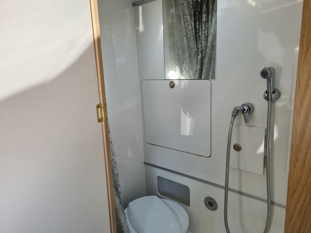 Mała biała łazienka w kamperze z toaletą, prysznicem ręcznym i lustrem.