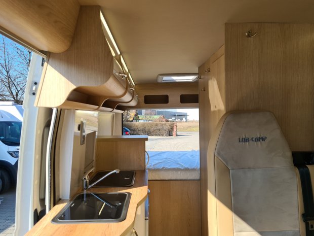 Wnętrze kampera z drewnianą zabudową, kuchenką z umywalką i tylnym łóżkiem