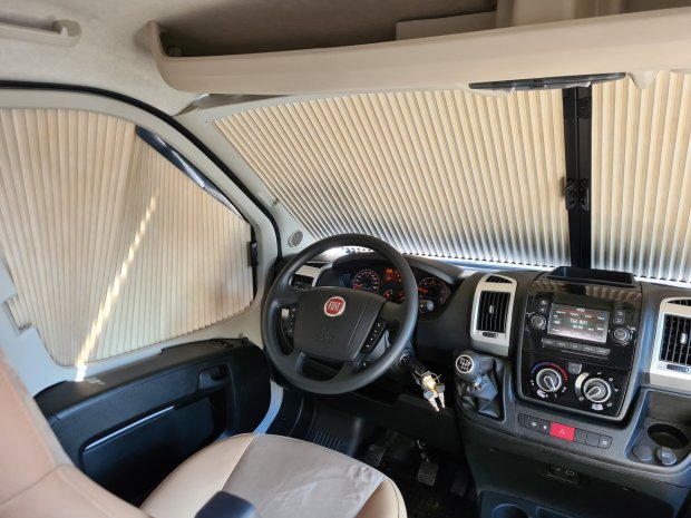 Kokpit Fiata z kierownicą, kluczykami i opuszczonymi beżowymi plisowanymi roletami.