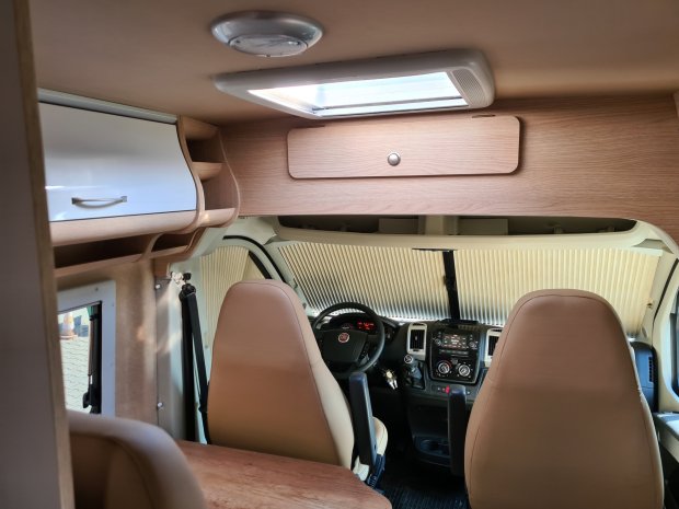 Wnętrze kampera: przednie fotele, kokpit i drewniane schowki nad kabiną