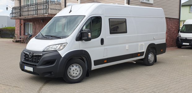 Biały dostawczy van zaparkowany przed domem z balkonem