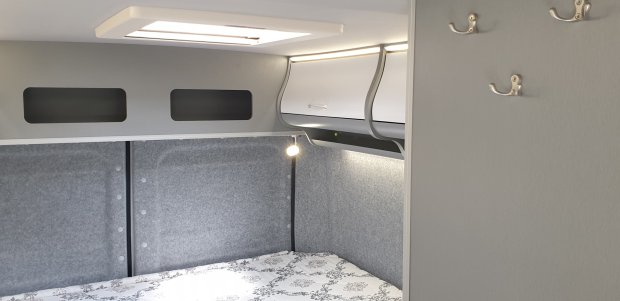 Wnętrze kampera: łóżko, górne szafki, szara wykładzina i lampka nocna
