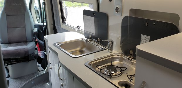 Wnętrze kampera: blat z umywalką i dwupalnikową kuchenką, obrotowe siedzenie kierowcy
