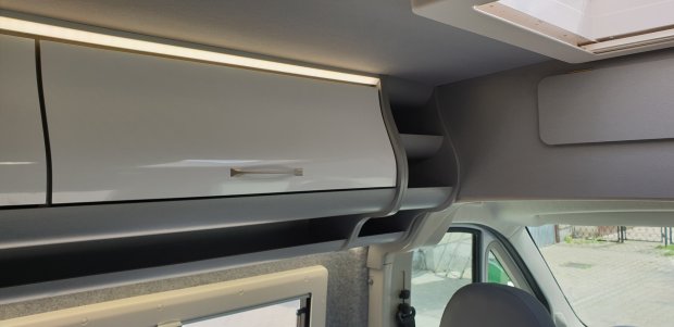 Białe górne szafki i półki nad kabiną w nowoczesnym kamperze