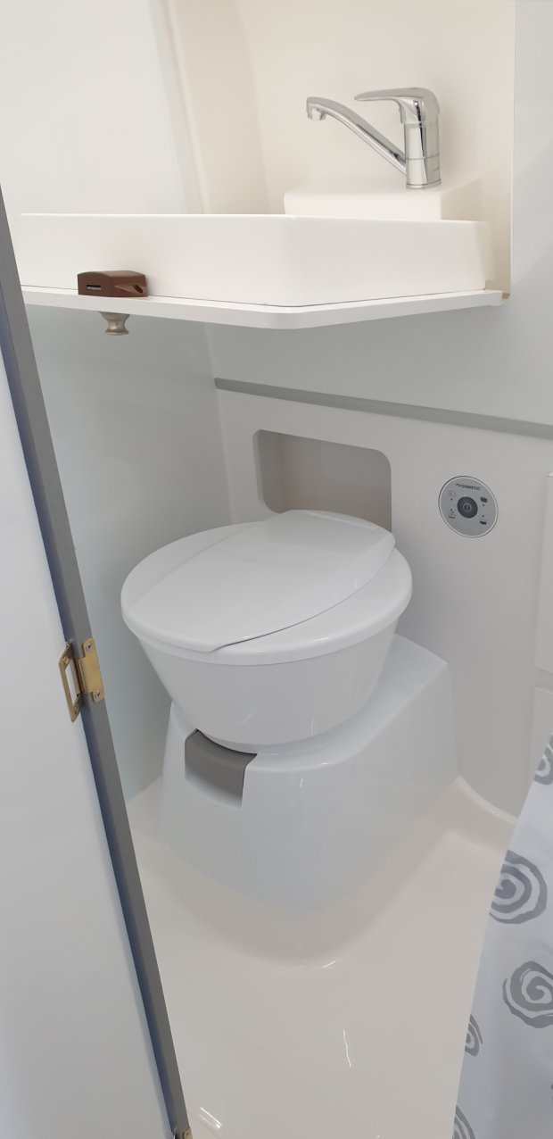 Kompaktowa biała toaleta w małej łazience z umywalką i chromowaną baterią