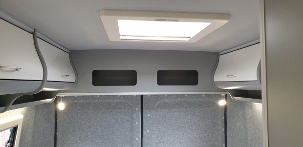 Wnętrze kampera: szare panele, białe górne szafki, świetlik w dachu i dwa kinkiety