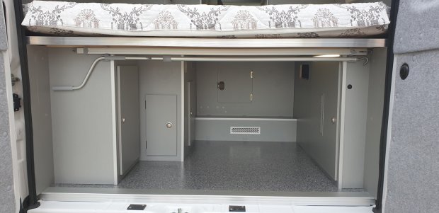 Schowek pod łóżkiem kampera z szarymi szafkami i materacem u góry