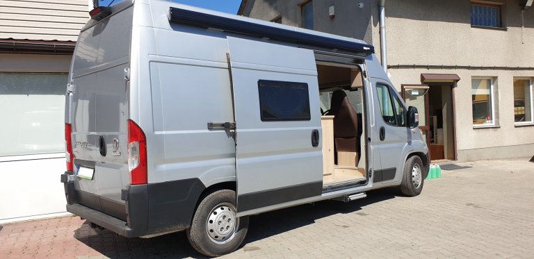 Srebrny campervan z otwartymi drzwiami przesuwnymi zaparkowany przy budynku