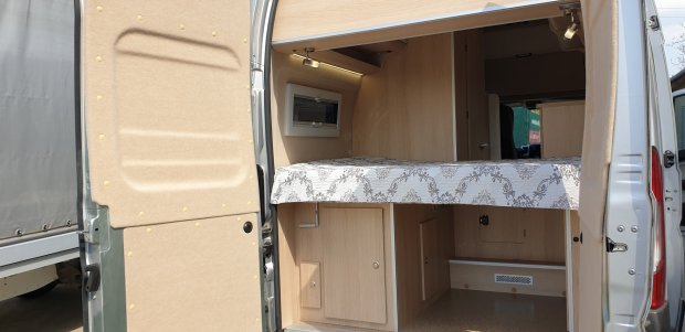 Wnętrze kampera z rozkładaną platformą sypialną i drewnianymi szafkami