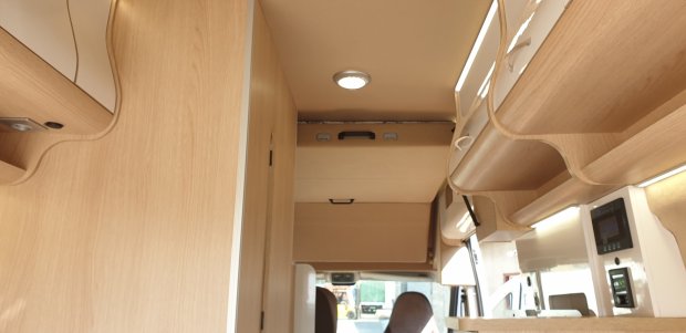 Wnętrze kampera z jasnymi drewnianymi szafkami sufitowymi i oświetleniem LED