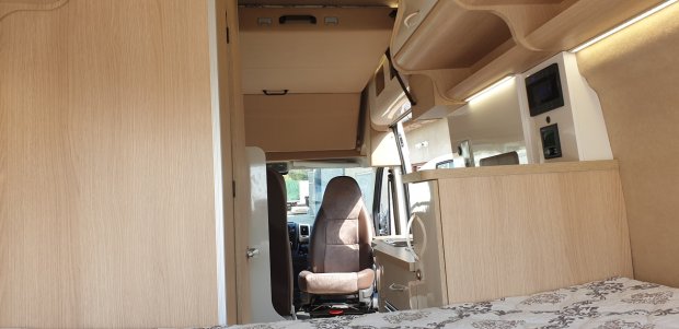 Wnętrze kampera z jasnymi drewnianymi meblami i brązowym fotelem kierowcy