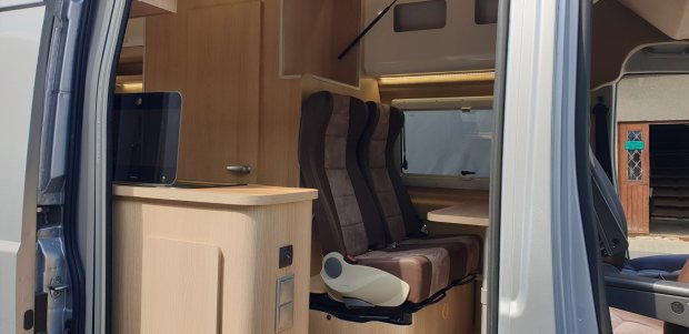 Wnętrze kampera przez otwarte drzwi z trzema brązowymi fotelami i drewnianą zabudową