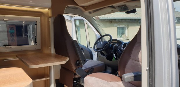 Wnętrze kampera z obracanymi fotelami, stołem i kokpitem kierowcy.