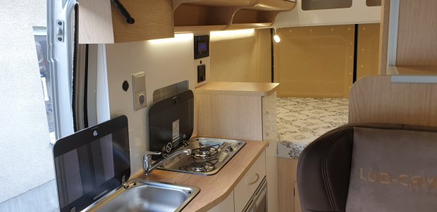 Wnętrze kampera: zlew i dwupalnikowa kuchenka na blacie, szafki i łóżko