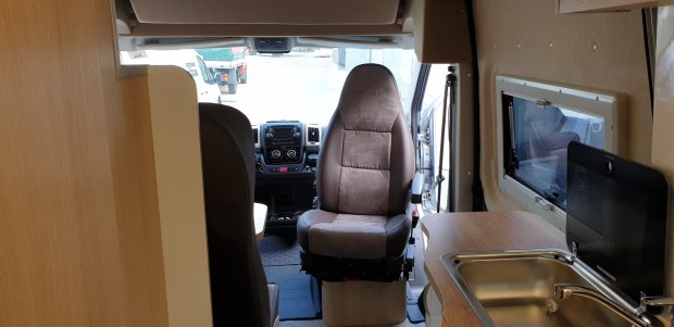Wnętrze kampera z obróconym fotelem pasażera, kokpitem i blatem kuchennym ze zlewem