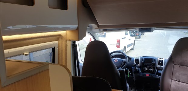 Wnętrze kampera: przednie fotele, kierownica i kokpit z widokiem na zaparkowany biały van.