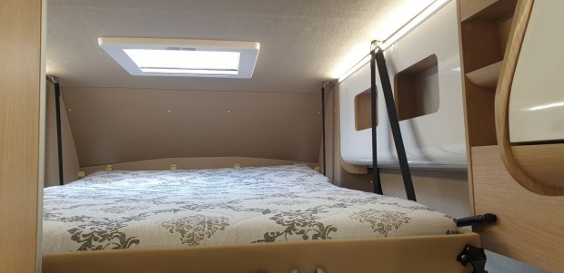 Przytulne łóżko w kamperze z dekorowanym materacem i świetlikiem.