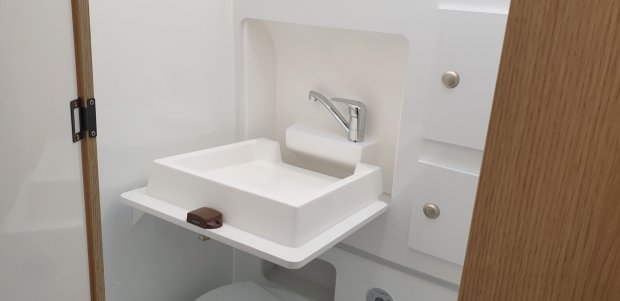 Składana biała umywalka z chromowaną baterią w małej kabinie