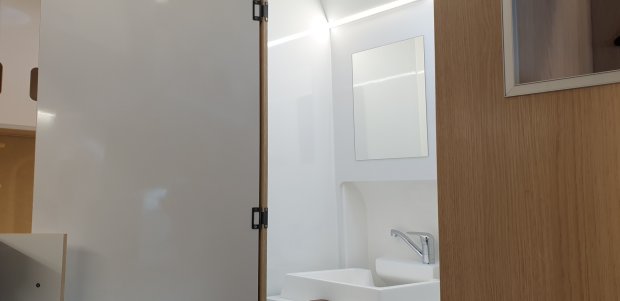 Umywalka i lustro w jasnej łazience widziane przez częściowo otwarte drzwi.