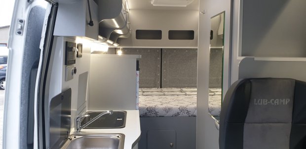 Wnętrze kampera z kuchnią (zlew, płyta), szafkami i łóżkiem