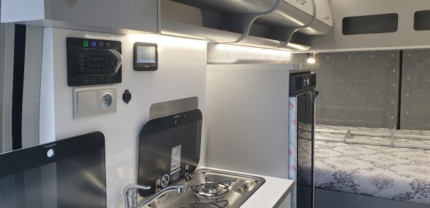 Wnętrze kampera: kompaktowa kuchnia z płytą gazową, zlewem i sypialnią w tle