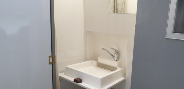 Mała biała umywalka z chromowaną baterią w ciasnej kabinie z szarą ścianą