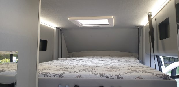 Sypialnia w kamperze: podwyższone łóżko z wzorzystym materacem i świetlikiem