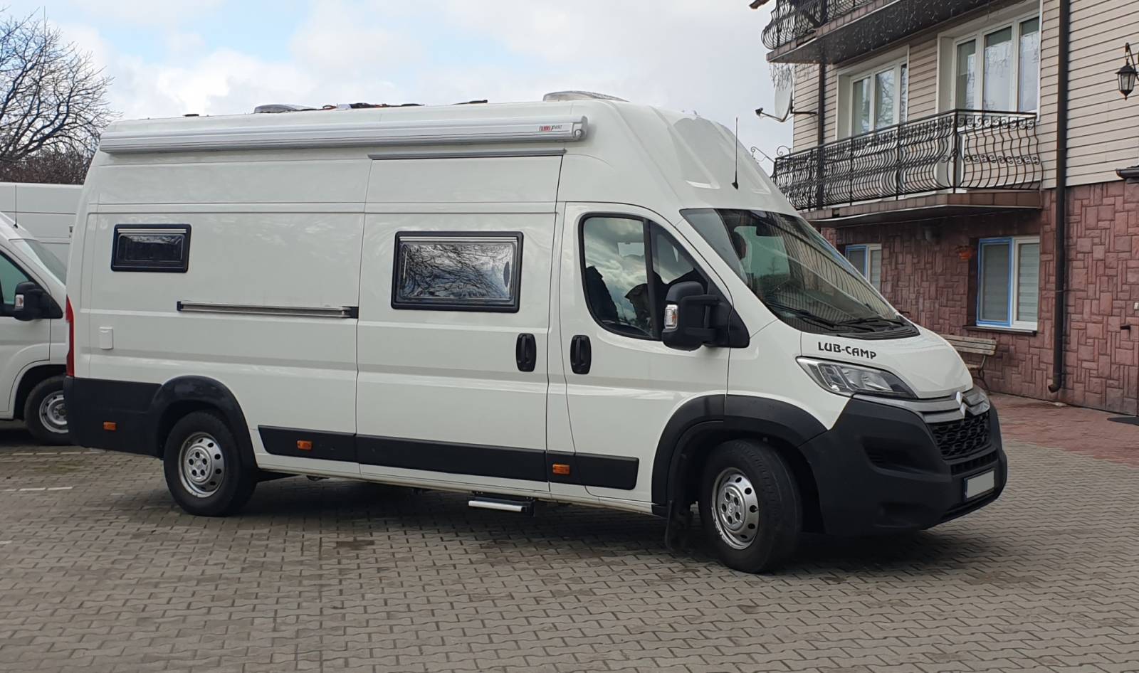 Biały kamper typu van zaparkowany obok budynku z balkonami