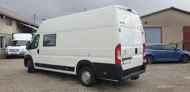 Biały kamper Citroën zaparkowany na placu przy budynkach.