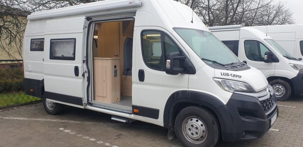 Biały kamper z otwartymi drzwiami bocznymi, widoczne wnętrze i schodek