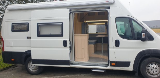 Biały camper z odsuniętymi drzwiami, widocznym wnętrzem z kanapą i szafką