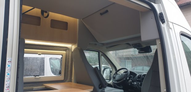Wnętrze kampera: fotele kierowcy i pasażera, stolik, okno z kroplami deszczu