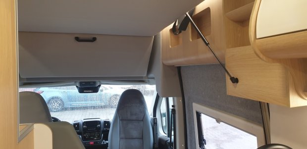 Wnętrze kampera z fotelem kierowcy, deską rozdzielczą i podnoszonym schowkiem nad kabiną